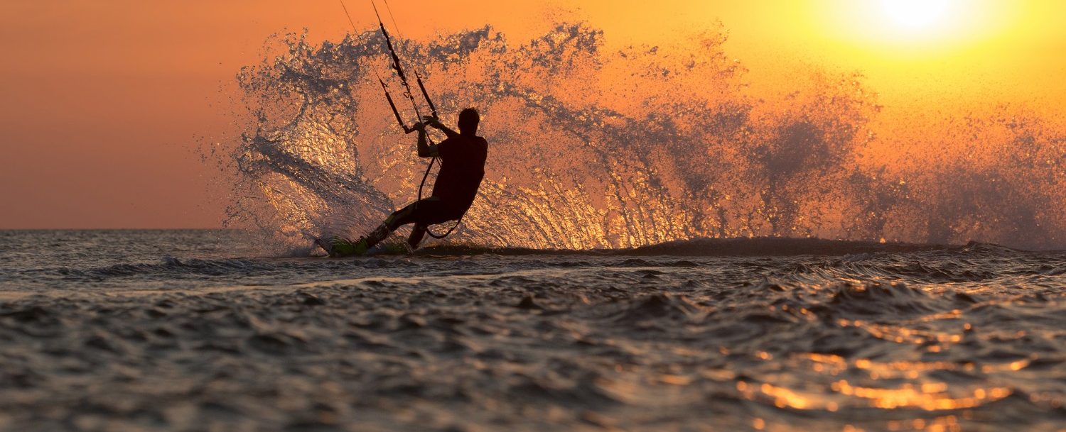 professional kiter makes the difficult trick on a beautiful background of spray and colourful sunset