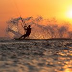 professional kiter makes the difficult trick on a beautiful background of spray and colourful sunset