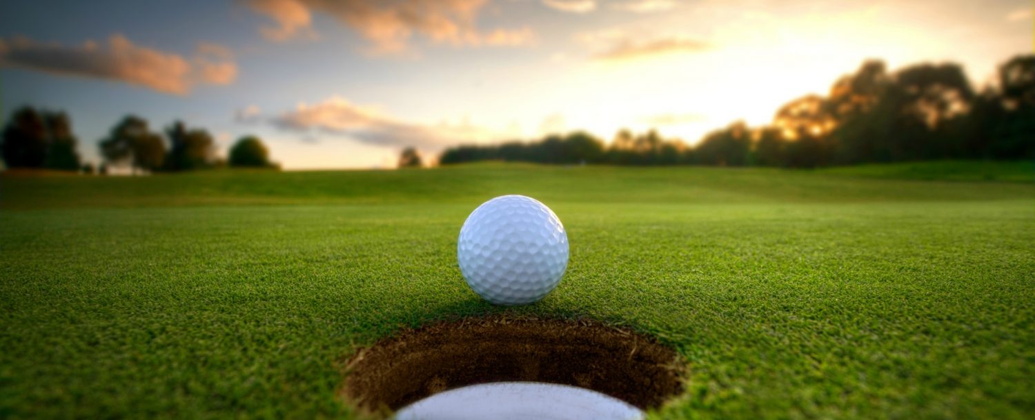 golf ball rolling into hole with beautiful sunset in the background