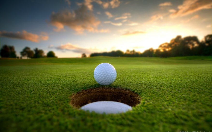 golf ball rolling into hole with beautiful sunset in the background