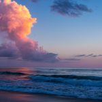 Amazing tall clouds over the ocean reflect the colors of the morning sun as it breaks over the horizon. Shades of purple, pink and blue in the sky and reflected on the water.