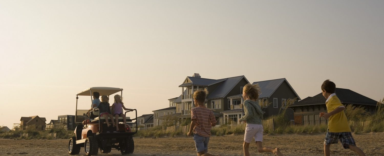 Kids running on the beach after a golf cart in the sand