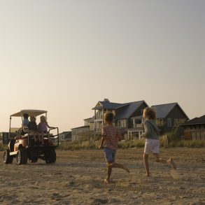 Kids running on the beach after a golf cart in the sand