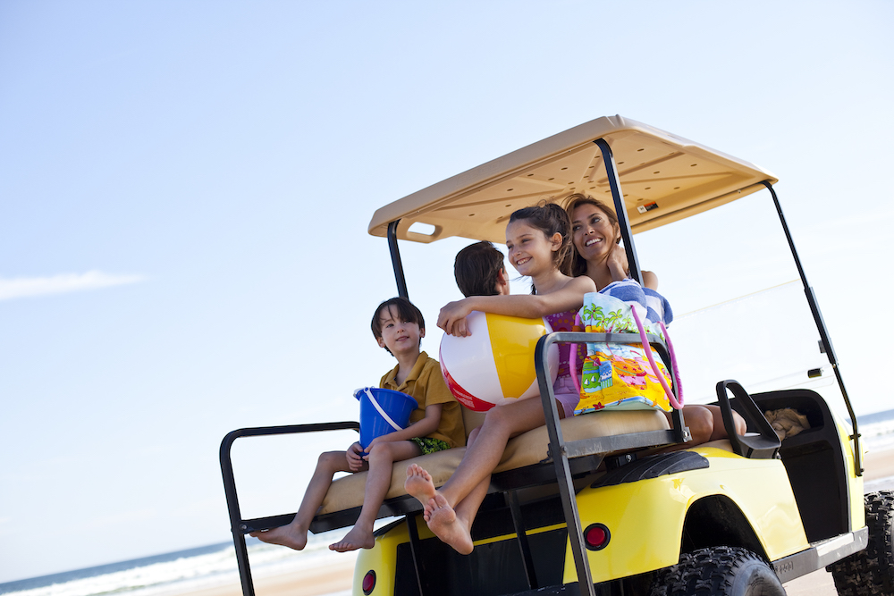 family heading to the beach in a golf cart. They have toys and beach bags in tow. 