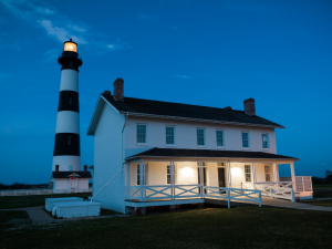 white and black stripe lighthouse with two-story historic house with porch