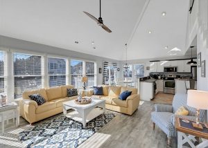 outer banks vacation rental living room with yellow couches, rug, coffee table, kitchen