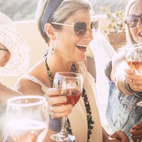 Closeup of happy beautiful cheerful people women celebrating together with red wine - bright sunny image joyful and friendship - young senior ladies smiling and laughing having fun at party