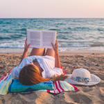 woman laying on beach reading a book