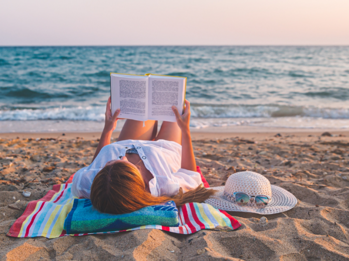 woman laying on beach reading a book