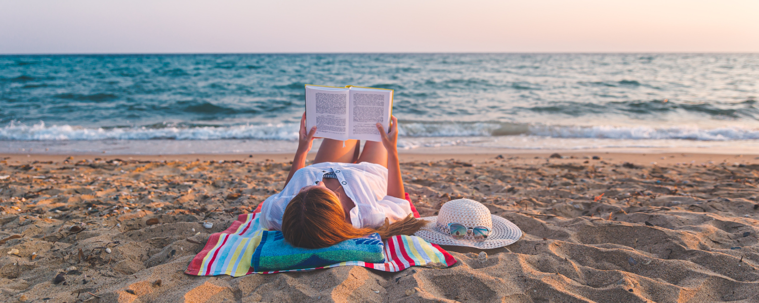 woman laying on beach reading a book