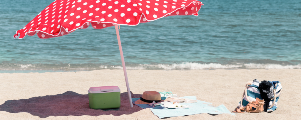 red beach umbrella, cooler, towel, hat on beach