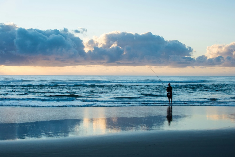 Silhouette of a man surf fishing on the beach