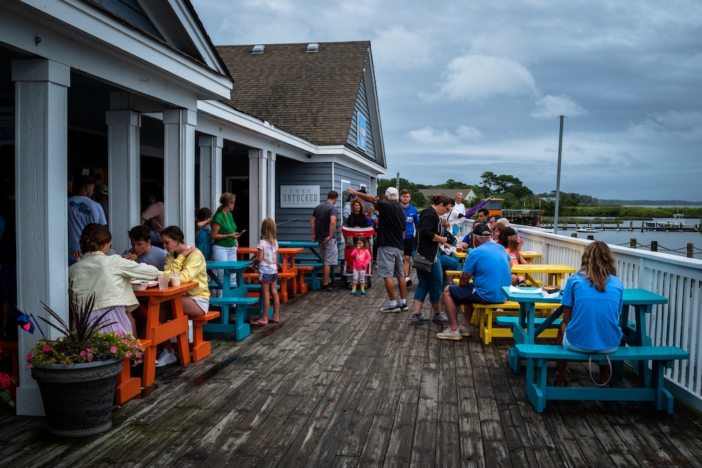A wide angle landscape photo of people having lunch on the boardwalk waterfront in Duck, NC.