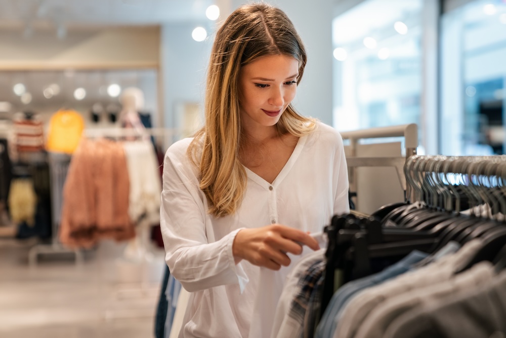 Happy young woman buying new clothes in store. 